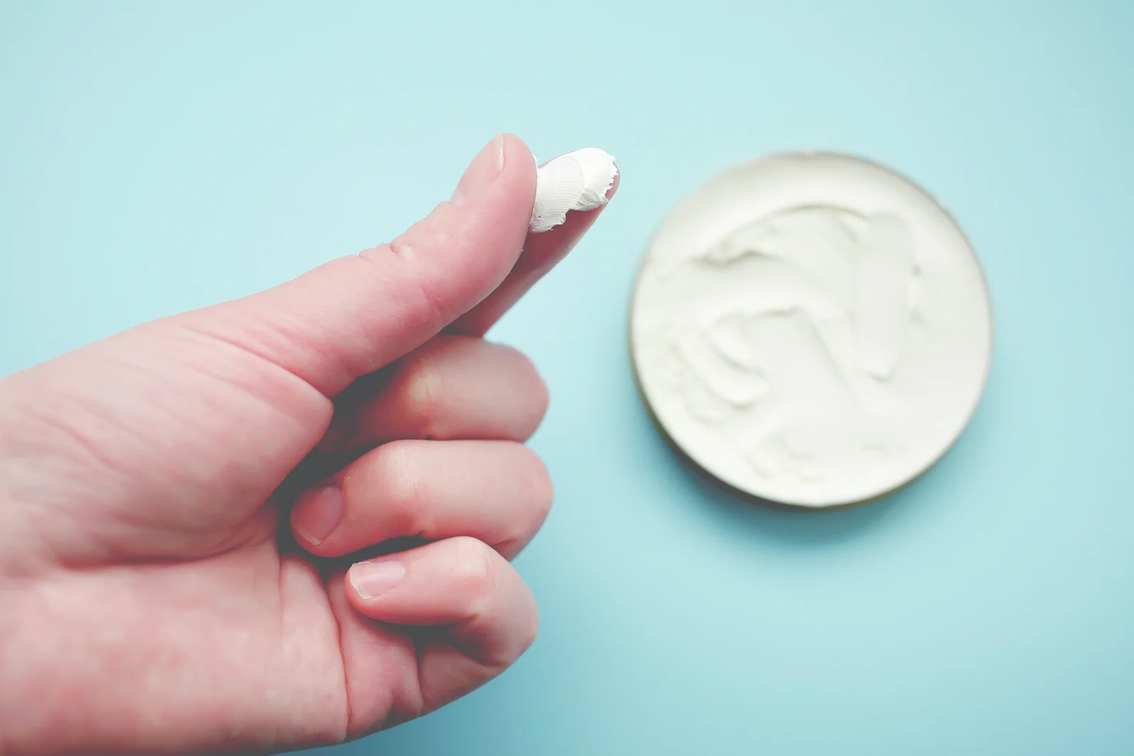 Ein Klecks Creme auf dem Finger, daneben der Tiegel